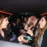 Ragazze e ragazzi si divertono sorseggiando prosecco in limousine